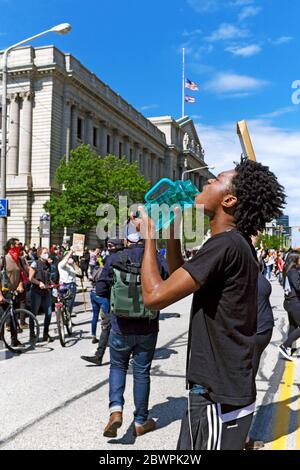 Un jeune homme noir se traite pour des gaz lacrymogènes par la police de Cleveland pendant le 30 mai 2020, Black Lives Matter protestation qui s'est transformée en ce qui a été appelé une émeute. L'homme noir a son dos à l'épicentre de la manifestation devenu émeute, le bâtiment du Cleveland Justice Center sur Lakeside Avenue dans le centre-ville de Cleveland, Ohio, États-Unis. Banque D'Images