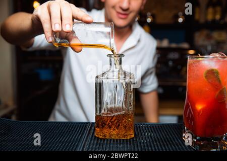 Le barman moure le whisky dans un décanteur transparent. Banque D'Images