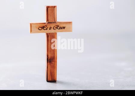 Croix en bois avec texte il est levé sur fond gris. Rappel du sacrifice de Jésus et de la résurrection du Christ. pâque de Pâques. Concept eucharistique Banque D'Images