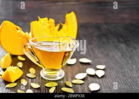 Huile de citrouille dans un saucière en verre, graines et tranches de légumes sur fond de bois Banque D'Images