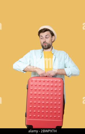 Un homme en chapeau et en veste soulève une lourde valise. Banque D'Images