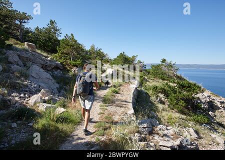 Homme grimpant des clifs avec son chien le long de la mer dans le matin d'été, Croatie Banque D'Images