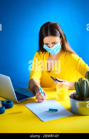 femme dans un chemisier jaune travaille à distance à la maison pendant une pandémie Banque D'Images