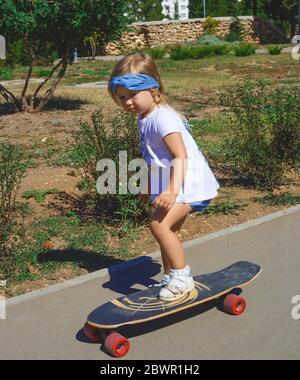 Une petite petite fille mignonne fait du skateboard dans le parc Banque D'Images