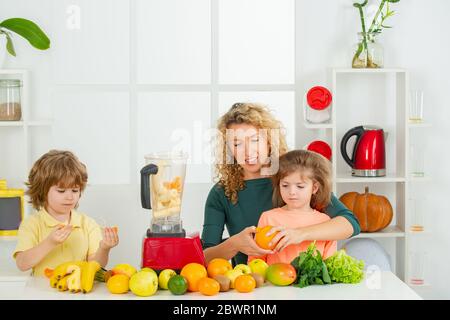 Maman fille et fils préparent un smoothie dans la cuisine. Famille heureuse et aimante. Une alimentation végétalienne et un mode de vie sain. Banque D'Images