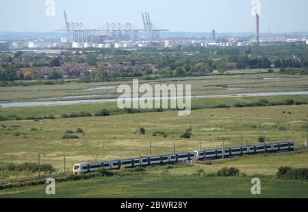 Un train C2C à Hadleigh, près de Southend, Essex, avec le DP World London Gateway Port et les réservoirs de stockage restants à l'ancienne usine de combustible de Coryton, près de Stanford-le-Hope en arrière-plan. Banque D'Images