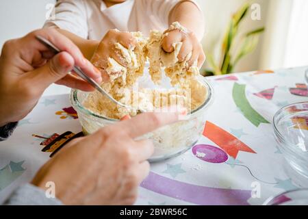 Une mère agite la pâte de farine alors que sa fille la pétrit avec ses mains. Ils font de la plasticine maison, le bol est assis sur une fête colorée
