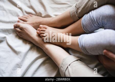 Gros plan des pieds de la mère et de l'enfant en train de frotter ensemble tout en étant assis sur des draps beige. C'est un moment intime et tendre.