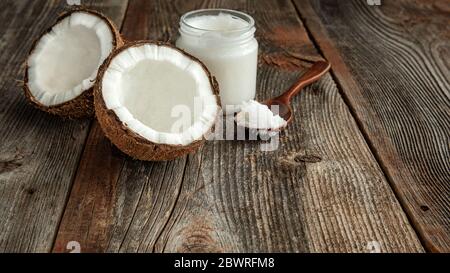 Deux moitiés de noix de coco, une cuillère et de l'huile de coco dans un pot sur une surface en bois. Le concept de nourriture saine. Banque D'Images