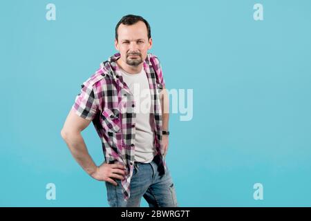 un jeune homme dans une chemise à carreaux, avec un chaume, regarde droit avec ses mains sur ses hanches et en se calant, essayant de voir quelque chose, mais sa mauvaise vue le fait Banque D'Images