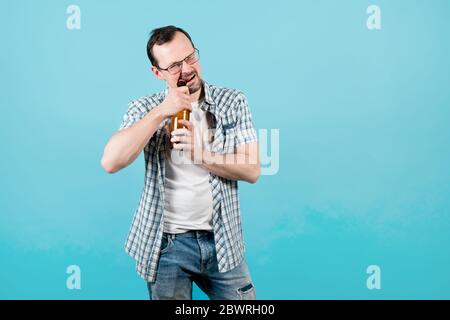 un homme dans une chemise à carreaux en lunettes ouvre un bouteille de bière avec ses dents Banque D'Images