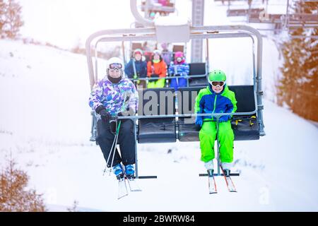 Garçon et fille s'assoient sur le télésiège de ski ensemble sur la station de montagne alpine vue d'un autre siège Banque D'Images