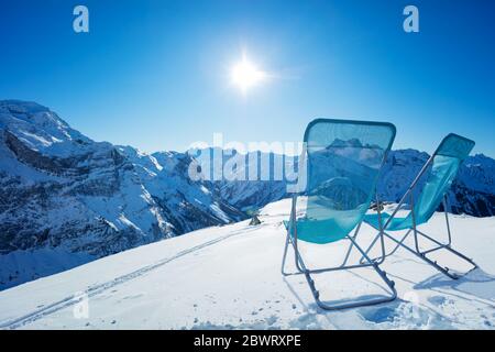 Deux chaises longues de chaise longue se tiennent sur la neige dans les montagnes au sommet enneigé par beau temps Banque D'Images