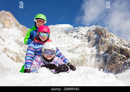 Portrait de trois enfants heureux couché l'un sur l'autre dans la neige souriant avec des montagnes sur le fond Banque D'Images