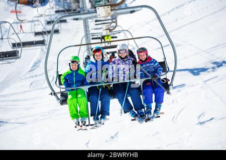 Groupe de skieurs les enfants s'assoient sur le télésiège en allant sur la montagne pour skier, assis ensemble souriant Banque D'Images