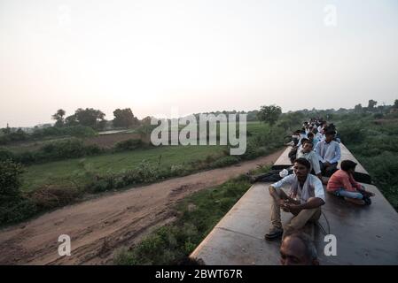 Des hommes au sommet d'un train surpeuplé traversant la campagne dans le Madhya Pradesh, en Inde. Chemins de fer indiens. Banque D'Images