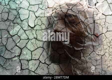 homme adulte couverture de visage par plastique avec crack sécheresse effet de sol dans la pollution de l'environnement ou psychologie concept de problème Banque D'Images