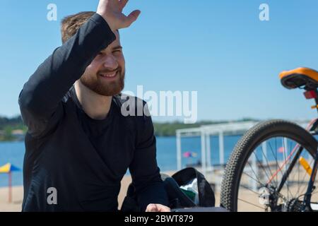 Joyeux cycliste barbu jeune gars en agitant, sur le fond d'un vélo. Extérieur. Sports de printemps. Le gars a vingt-cinq ans. Vélo de printemps Banque D'Images