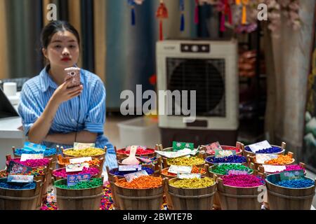 Chongqing, Chine - août 2019 : femme chinoise ennuyée assise dans un magasin de rue vendant des épices étranges et colorées et d'autres ingrédients alimentaires, C Banque D'Images