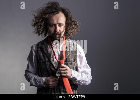 studio portrait en mouvement d'un jeune homme barbu, bourré et bourré de trente ans, dans un gilet de plaid, et une cravate rouge volant, agitant de longs cheveux. Sur un bac gris Banque D'Images