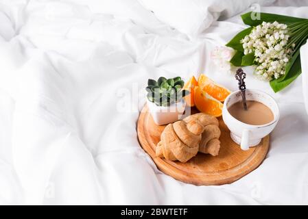 Café avec du lait et un bouquet de lys de la vallée dans le lit avec un croissant et une orange. Un lieu pour le texte Banque D'Images