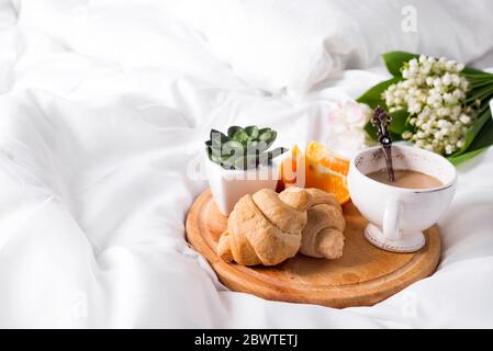 Café avec du lait et un bouquet de lys de la vallée dans le lit avec un croissant et une orange. Petit-déjeuner au lit le matin, un lieu pour le texte Banque D'Images