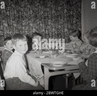 Années 1960, histoire, jeunes enfants assis à l'intérieur à une table lors d'une fête d'anniversaire, Angleterre, Royaume-Uni. Banque D'Images