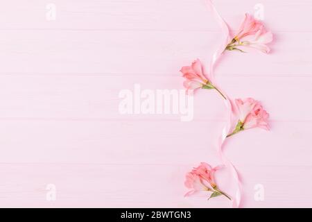 Composition florale de dessus plat de belles bourgeons de fleurs d'alstroemeria et ruban de soie sur fond rose avec espace de copie. Banque D'Images