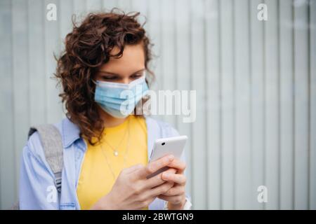 Portrait jeune femme portant un masque de protection médical tenant son smartphone à l'extérieur. Banque D'Images