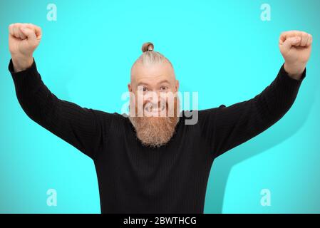 Homme heureux et chanceux qui célèbre la victoire isolé sur fond bleu. Un gars barbu plein de joie, motivé par le succès qui se hante les poings regardant la caméra Banque D'Images