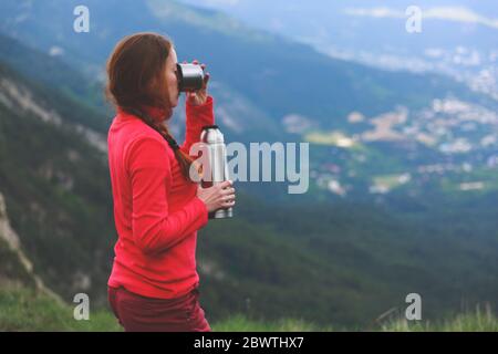 Gros plan d'une tasse avec thé dans la main du voyageur hors de la vue de la montagne. Une jeune touriste boit une boisson chaude d'une tasse et apprécie le paysage dans les montagnes. Concept de trekking Banque D'Images