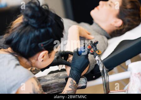 Tatoueur de femme tatouant sur le bras d'une femme Banque D'Images