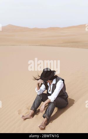 Jeune femme à la mode assise pieds nus sur une dune, désert de Merzouga, Maroc Banque D'Images