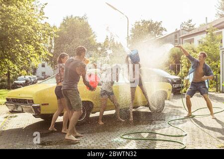 Groupe d'amis lavant la voiture jaune vintage en été s'amuser Banque D'Images