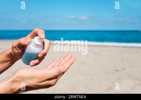 gros plan d'un homme caucasien sur la plage désinfectant ses mains avec un désinfectant bleu pour les mains d'une bouteille, avec l'océan en arrière-plan Banque D'Images