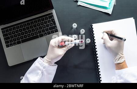 Médecin avec écriture d'échantillons COVID-19 sur ordinateur portable spirale au bureau en laboratoire Banque D'Images