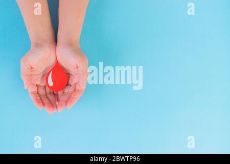 Don de sang mondial et Journée de l'hémophilie. Mains de femme tenant une goutte de sang rouge. Vue de dessus avec espace de copie. Banque D'Images
