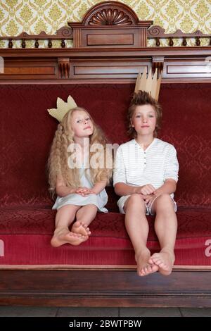 Garçon et fille assis sur un canapé portant des couronnes en carton Banque D'Images