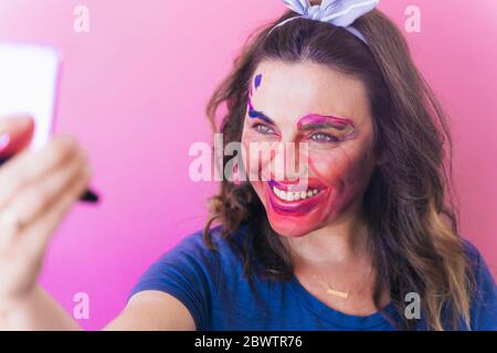 Femme regardant sa peinture de visage de coloful dans un miroir Banque D'Images