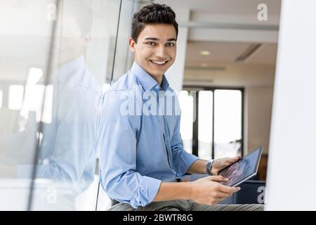 Portrait d'un jeune homme d'affaires souriant avec une tablette à la fenêtre du bureau Banque D'Images