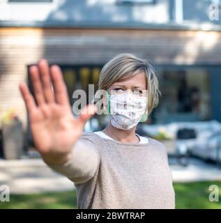 Portrait d'une femme portant un masque facial de protection debout avec un geste d'arrêt contre la maison pendant l'isolement Banque D'Images