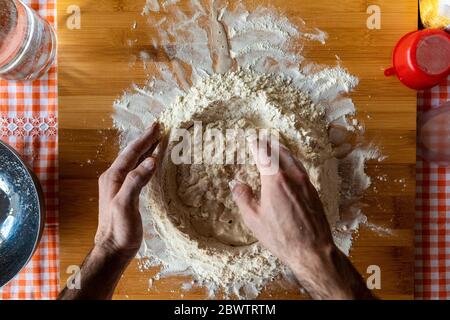 Mains d'homme préparant de la pâte sur un panneau en bois, vue de dessus Banque D'Images