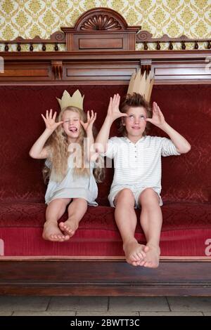 Garçon et fille assis sur un canapé portant des couronnes en carton qui s'en déchetent Banque D'Images