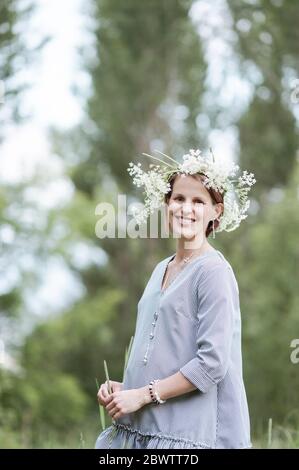 Femme enceinte souriante portant des fleurs debout dans le parc Banque D'Images