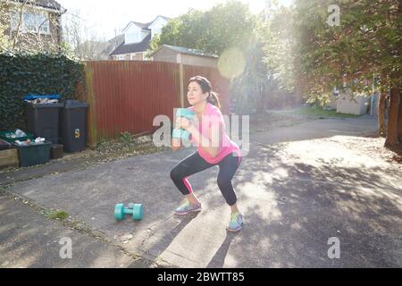 Pleine longueur de femme pratiquant des squats avec des haltères dans la cour arrière le jour ensoleillé Banque D'Images