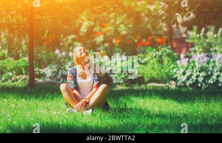 Bonne jeune femme libre assis à l'extérieur en position de yoga avec les yeux fermés sur l'herbe de parc d'été calme fille appréciez le sourire et de se détendre dans l'air de la ville de printemps. Min Banque D'Images