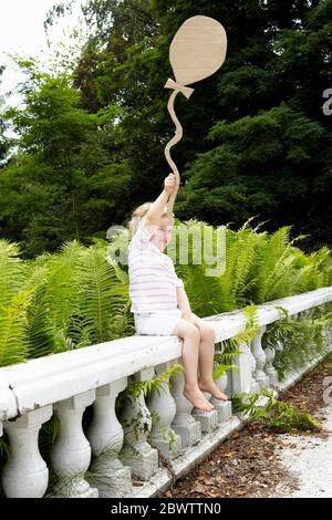 Petite fille assise sur une balustrade tenant un ballon en carton Banque D'Images