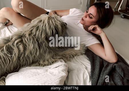 Femme mature couché sur le lit le matin jouant avec son chien Banque D'Images