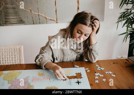 Femme confondue jouant avec puzzle à la table pendant la quarantaine à la maison Banque D'Images