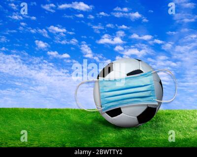 Rendu 3D, ballon de football recouvert d'un masque chirurgical sur le terrain de football Banque D'Images